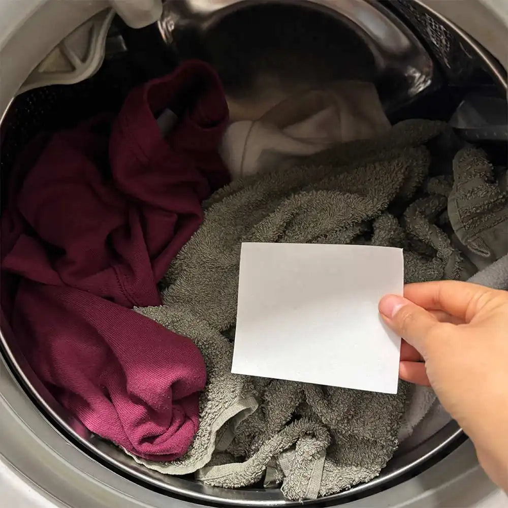 Gros plan sur une main qui mets la lessive en feuille sur le linge sale dans le lave-linge – démonstration du mode d’emploi.